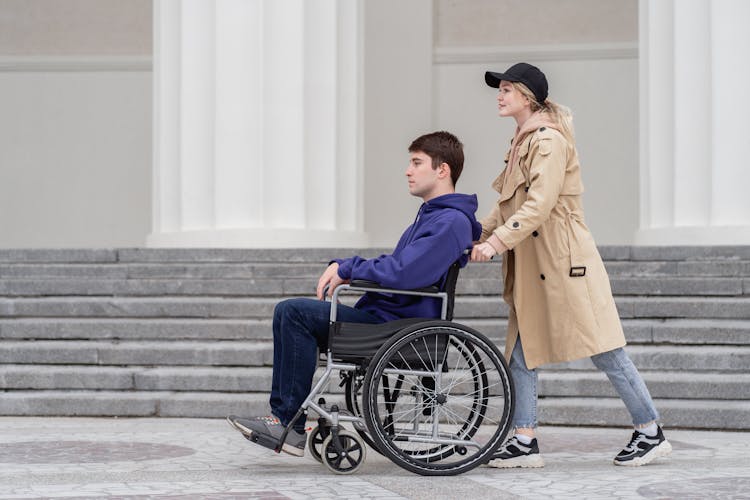 Woman Pushing A Man Sitting On A Wheelchair