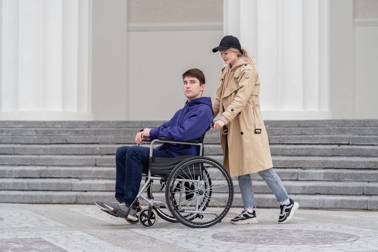 A Woman Pushing A Wheelchair With Man