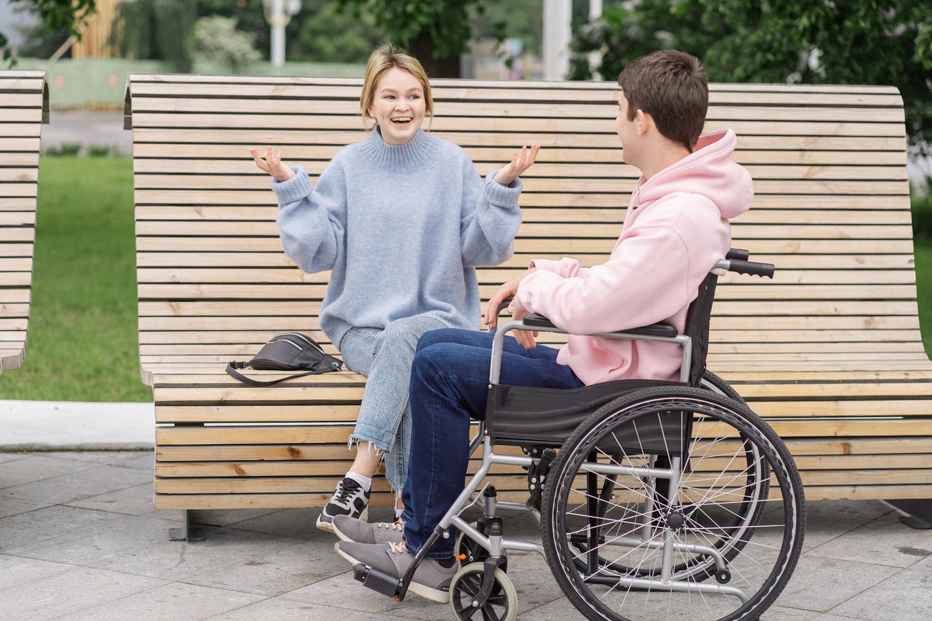 Smiling couple enjoying conversation on a wooden bench outdoors. Inclusive and friendly atmosphere.