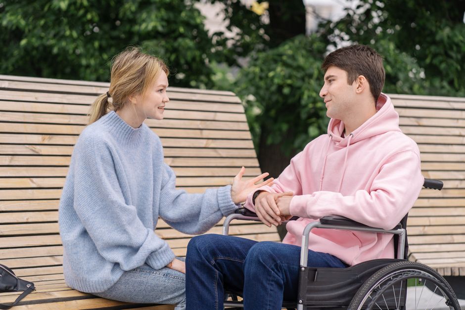 Young adults engaging in a warm conversation outdoors, one in a wheelchair.