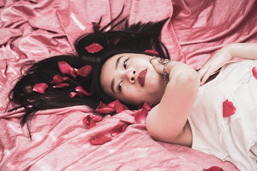 Free A Woman in White Tank Top Lying Down with Petals on Her Hair Stock Photo