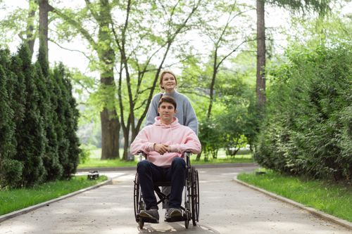 Free A couple enjoying a sunny day in the park, one in a wheelchair, pushing forward with a smile. Stock Photo