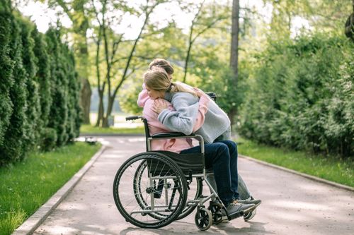 Free A couple lovingly embraces on a sunny day in a park, with one using a wheelchair. Stock Photo