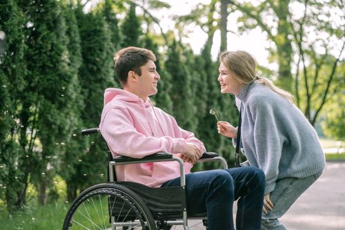 Free A young man in a wheelchair enjoys a cheerful moment with a woman outdoors. Stock Photo