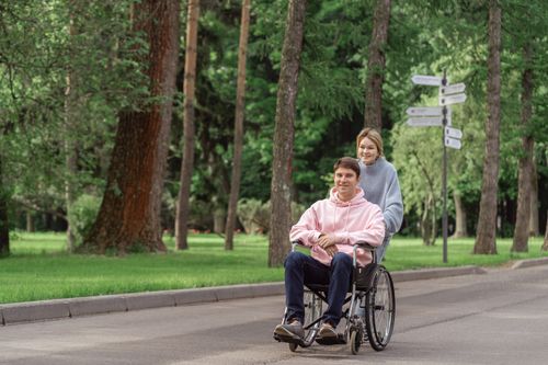 Free Happy couple enjoying a sunny day outdoors, with a woman pushing a man in a wheelchair. Stock Photo