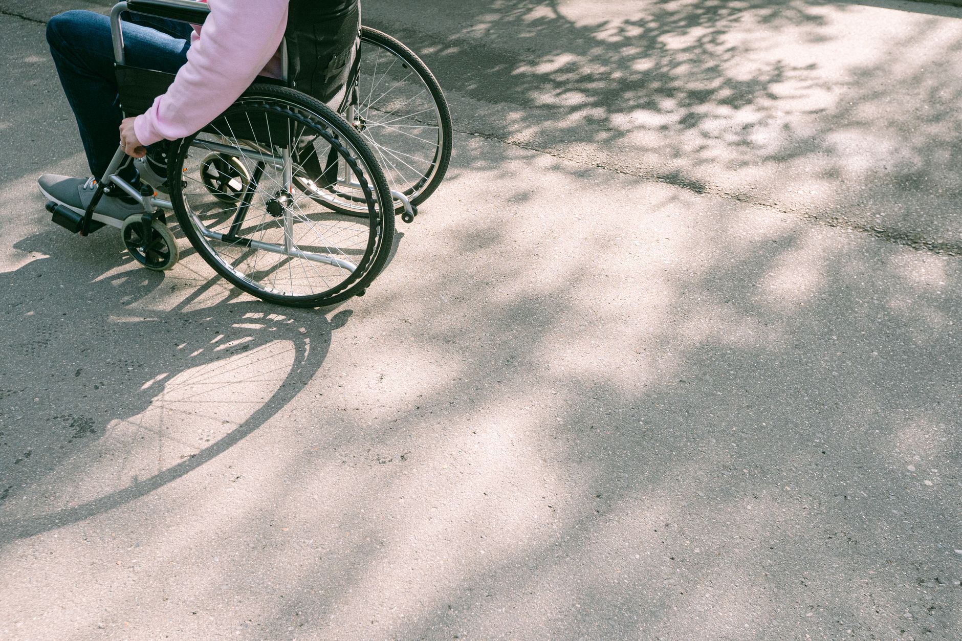 A person in a wheelchair navigating a sunlit road with tree shadows. The image captures a moment of mobility and independence.