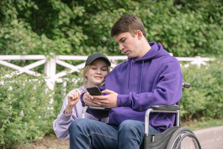 Man On A Wheelchair And Woman Looking At A Smartphone Screen 