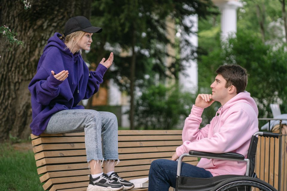 Two young people in hoodies talking on a park bench