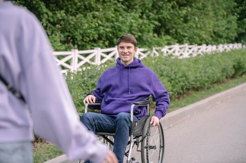 Free Portrait of a man in a wheelchair wearing a purple hoodie, smiling outdoors. Stock Photo