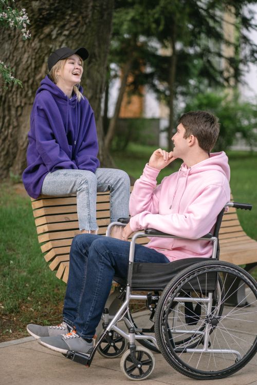 Free A young couple enjoying a cheerful conversation outdoors, dressed casually with a wheelchair in view. Stock Photo