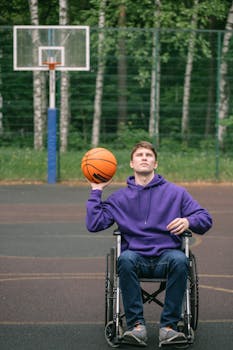Young man in wheelchair playing basketball on an outdoor court, displaying determination and skill.