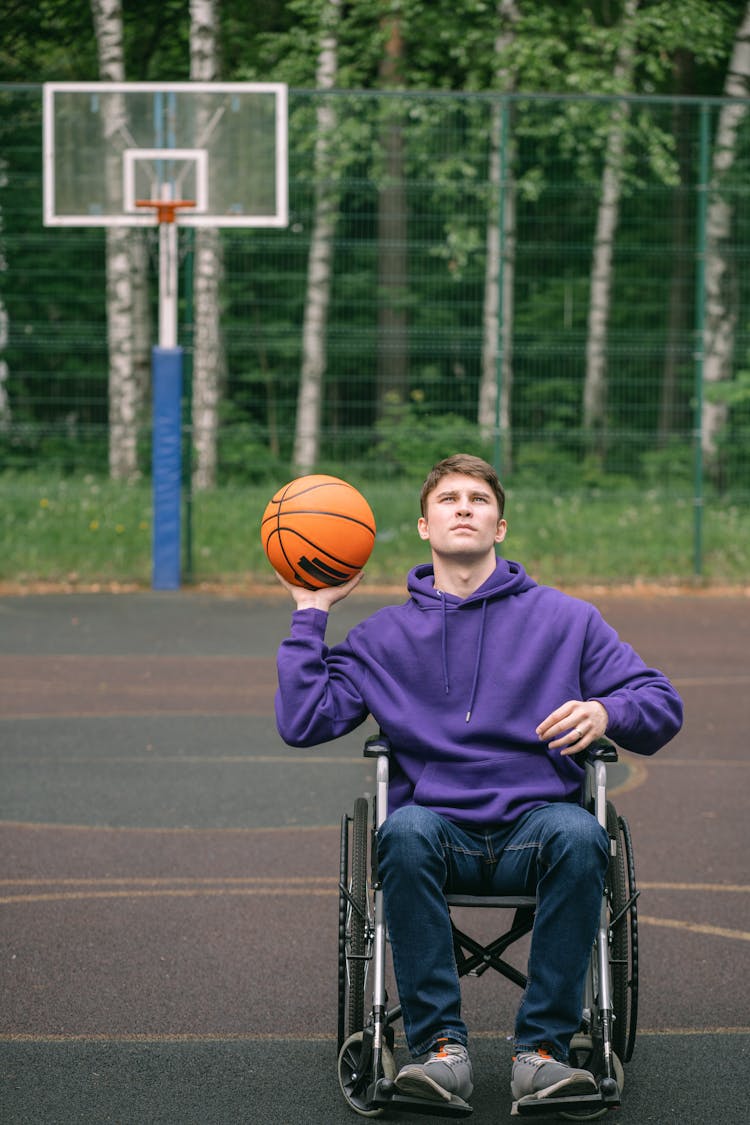 A Man Sitting On The Wheelchair Holding A Ball