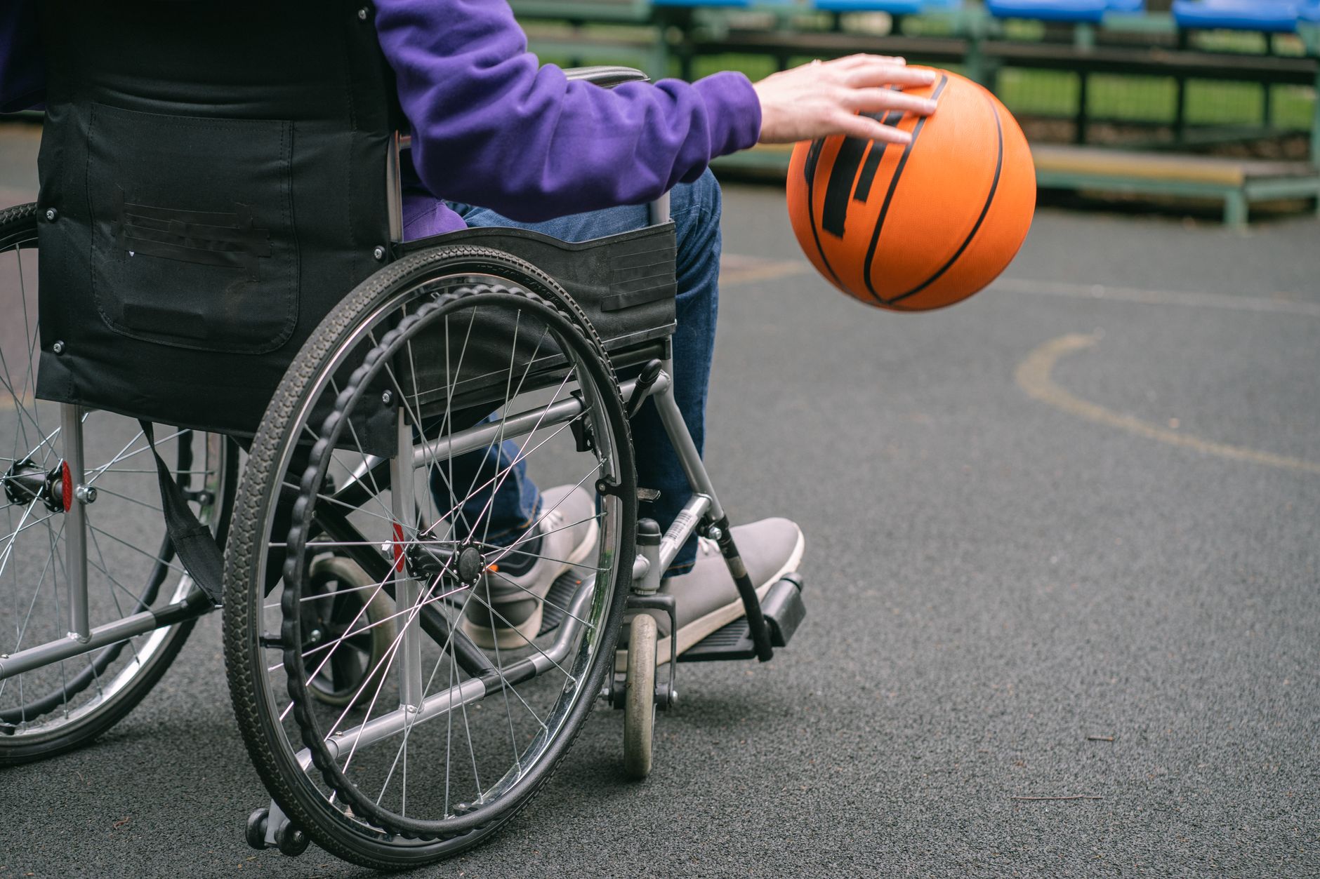 Close-up of a person in a wheelchair playing basketball outdoors, highlighting inclusivity and sports spirit.