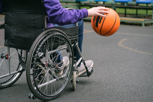Close-up of a person in a wheelchair playing basketball outdoors, highlighting inclusivity and sports spirit.
