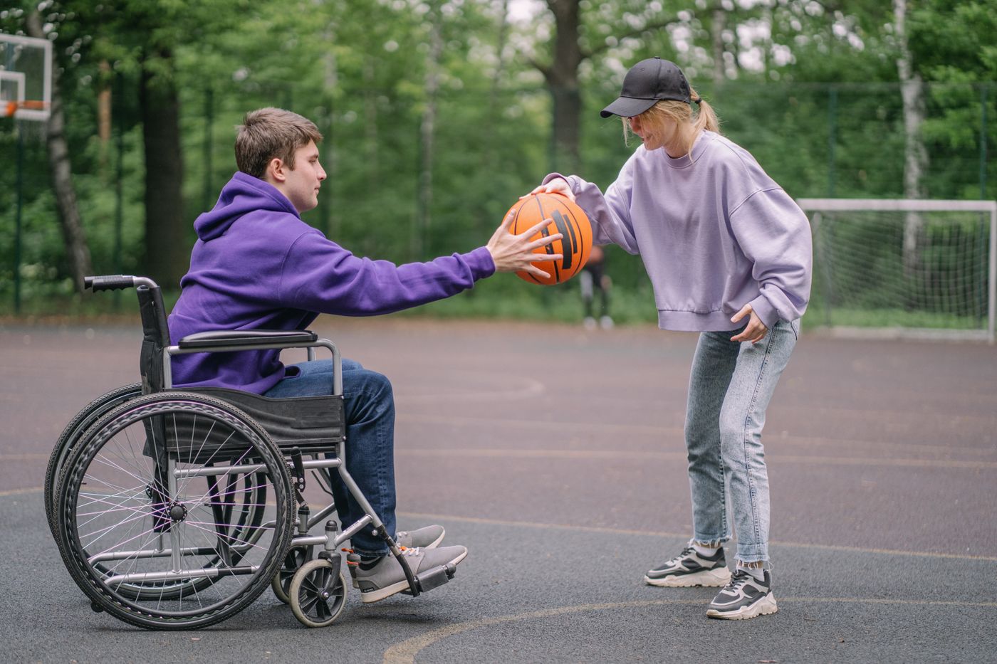 A Spinel Care support worker and a young NDIS participant who uses a wheelchair playing basketball together at an outdoor community court