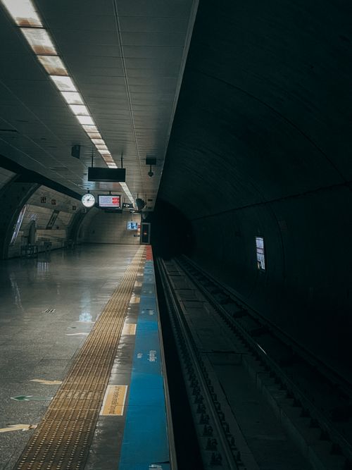 Free A deserted subway station platform with tracks disappearing into a dark tunnel, illuminated signs and tiles. Stock Photo