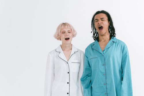 Free Two adults in pajamas yawning, expressing tiredness and sleepiness indoors. Stock Photo