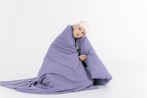 Free A woman with colored hair wrapped in a purple blanket, sitting on a white background, exuding warmth and comfort. Stock Photo
