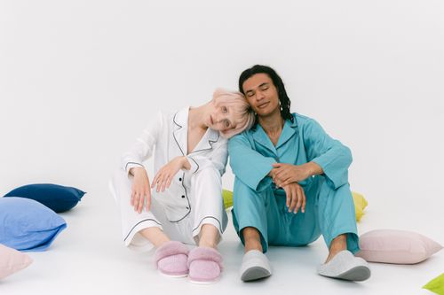 Free Couple in pajamas resting against each other with colorful pillows around them. Stock Photo
