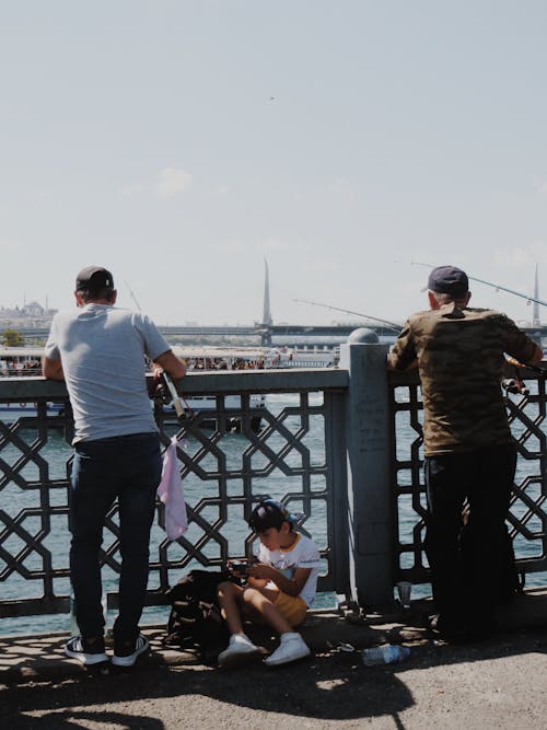 Back View Shot of Men Fishing while Leaning on a Concrete Fence