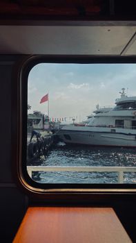 Serene scene of a luxurious yacht docked at a harbor, viewed through a window.