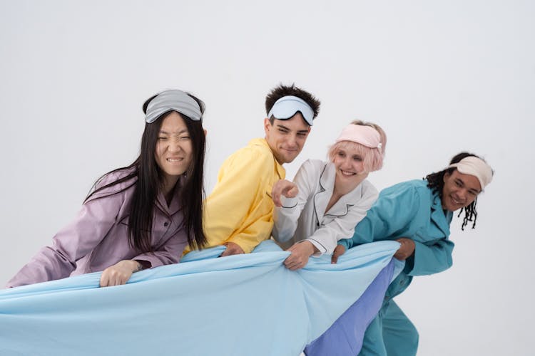 A Group Of People Pulling A Blue Blanket With Sleeping Mask On Their Heads