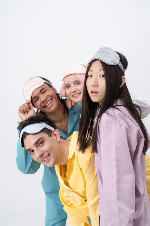 Free Group of diverse friends wearing colorful sleepwear and masks, laughing indoors. Stock Photo