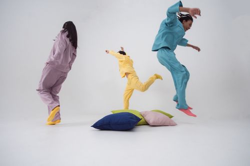 Free Group of adults in colorful pajamas jumping over pillows indoors, enjoying playful activities. Stock Photo
