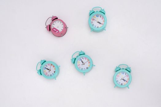 Five colorful analog alarm clocks arranged on a white background in a minimalist setup.