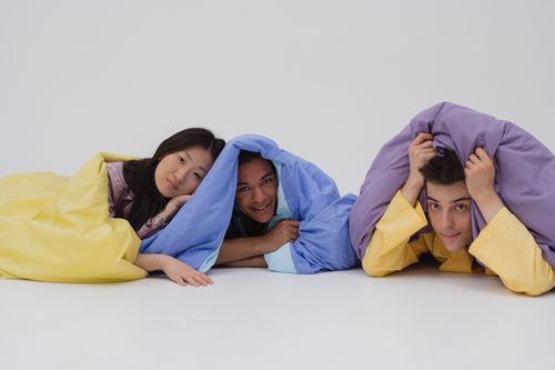 Free Diverse group of young friends smiling while lying under colorful blankets, evoking warmth and friendship. Stock Photo