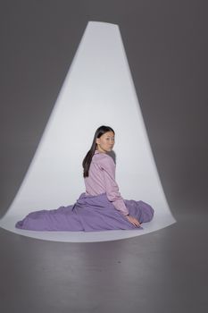 An Asian woman with long hair in purple sleepwear sitting on the floor, looking back.