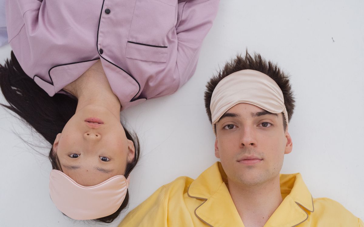 A man and woman lying on a white surface wearing pajamas and sleep masks.