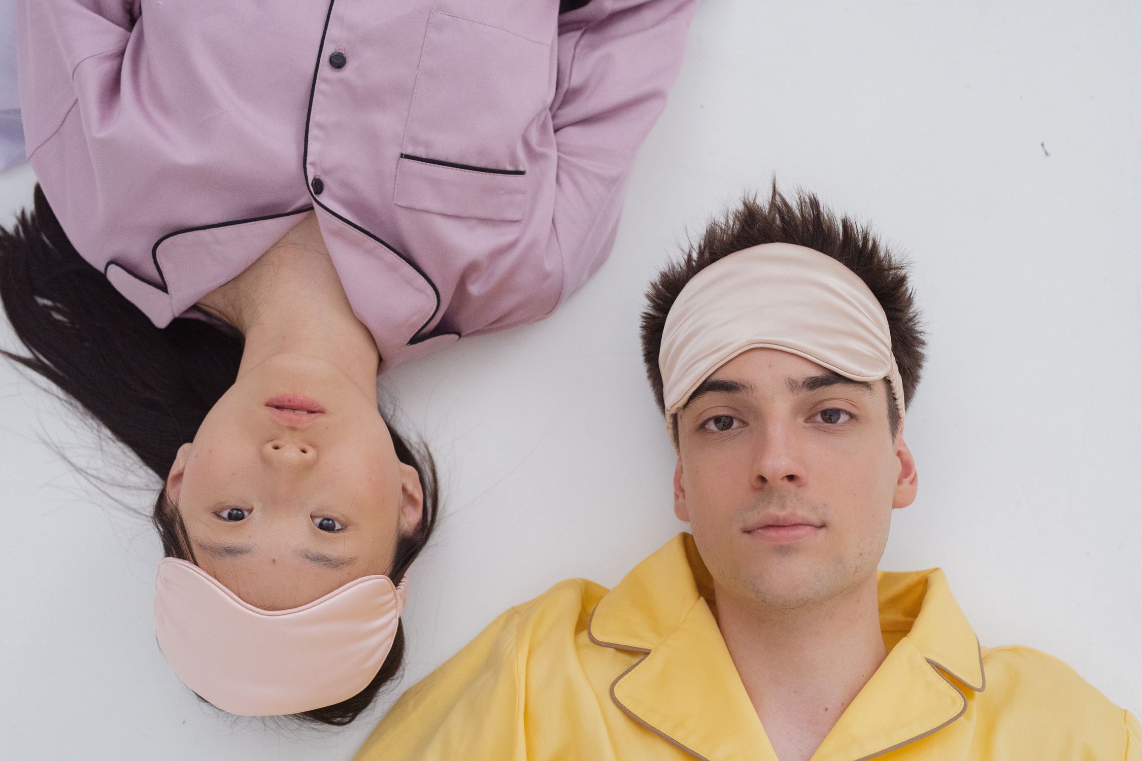 A man and woman lying on a white surface wearing pajamas and sleep masks.
