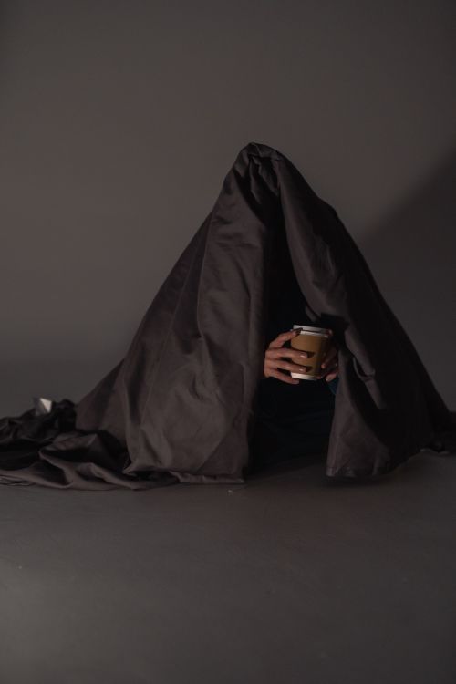 Free A person under a dark blanket holding a paper cup in a relaxing setting. Stock Photo