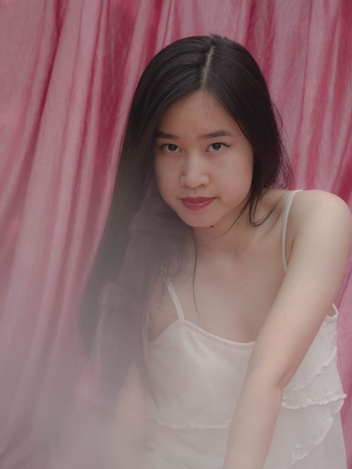 Free Portrait of a young woman in a delicate dress against a pink backdrop, embodying grace and elegance. Stock Photo