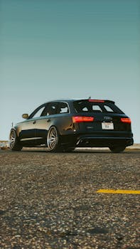 Black Audi station wagon parked on an asphalt road, showcasing speed and elegance in outdoor light.