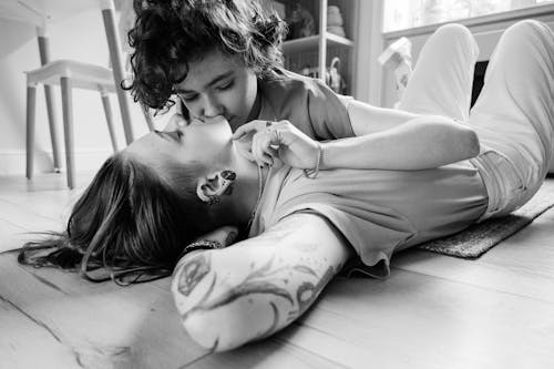 A Grayscale Photo of a Woman Kissing Her Partner Lying on the Floor