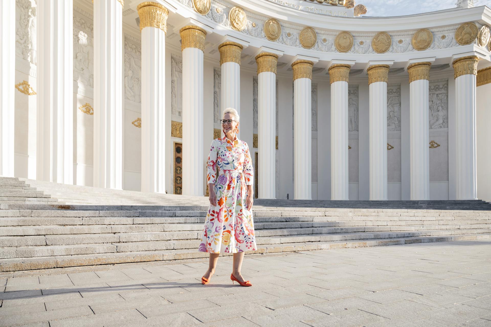 A stylish senior woman standing confidently in front of a grand neoclassical building.