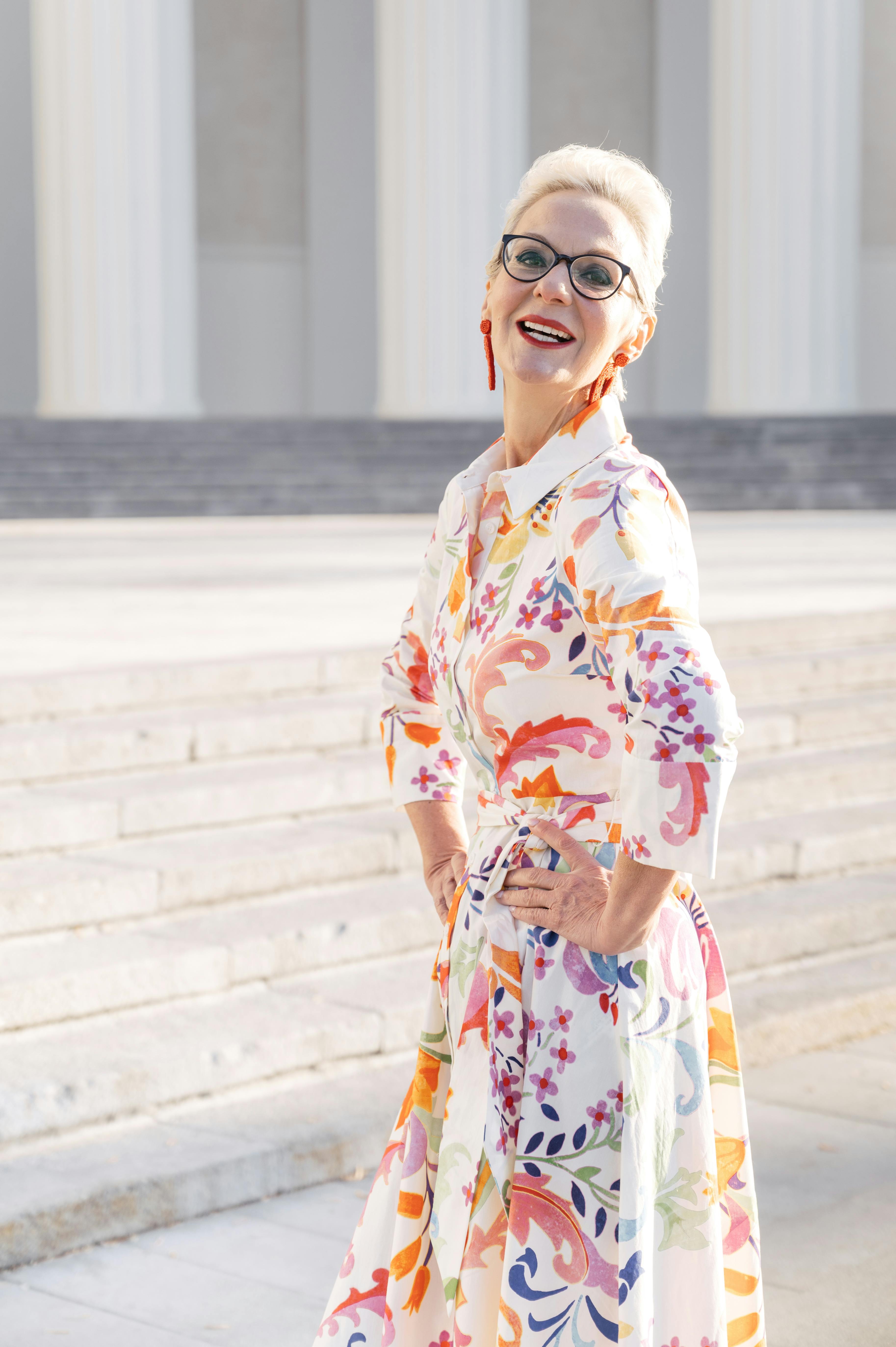 an elderly woman in printed dress smiling with her hands on her waist