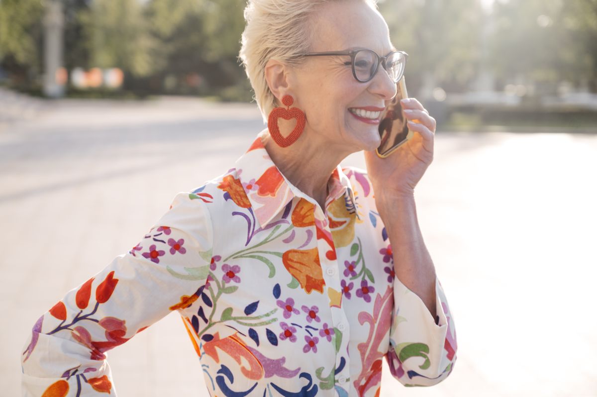 A smiling older woman on a phone call outdoors, setting up her ride preferences