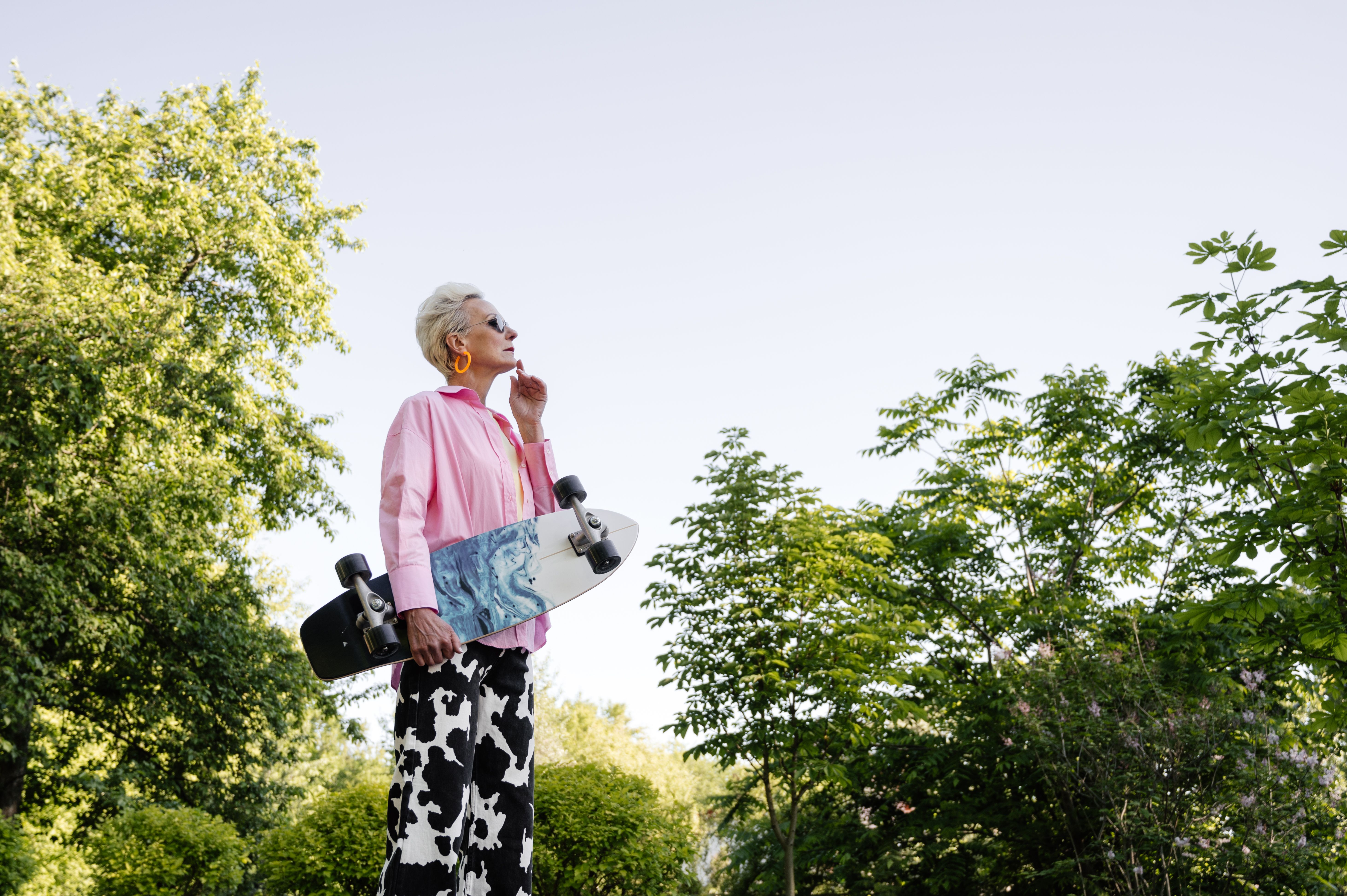 Stylish senior woman posing with skateboard in a lush green park, embracing an active lifestyle.