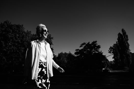 Elegant senior woman wearing sunglasses, enjoying a sunny day in a monochrome setting.