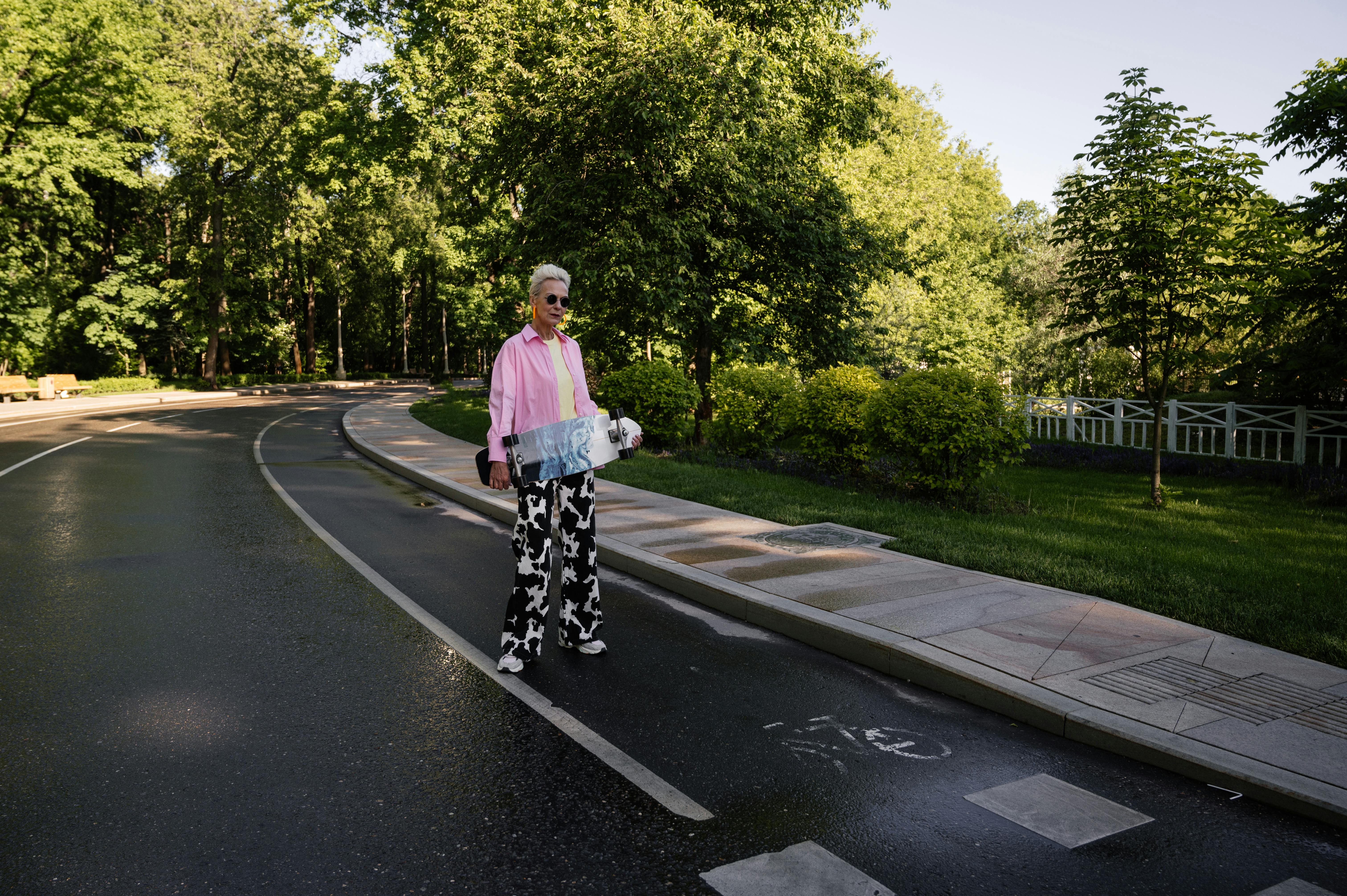 woman standing on roadside holding a skateboard