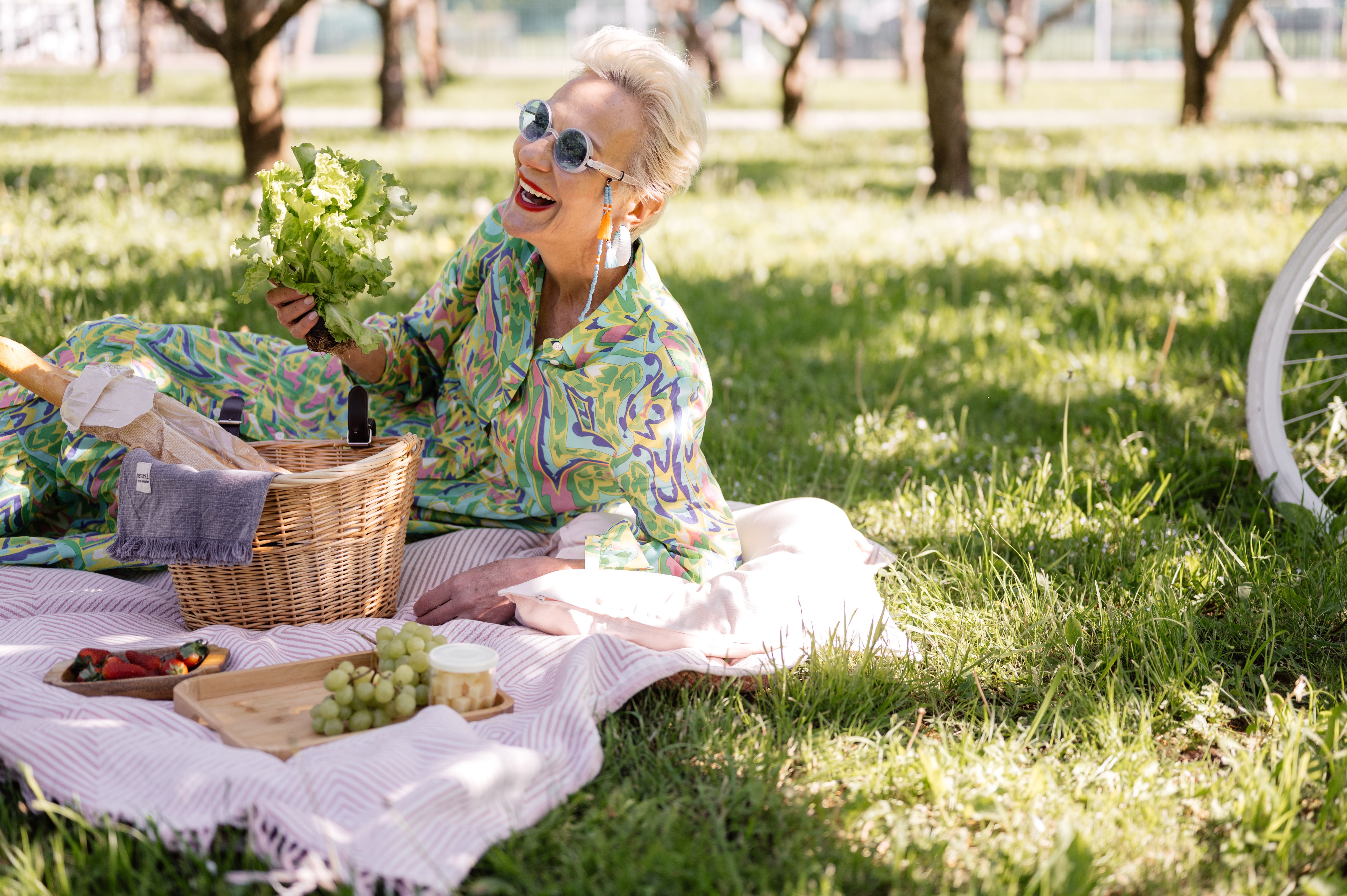 Elderly woman enjoying a picnic with vibrant clothing and fresh greenery.