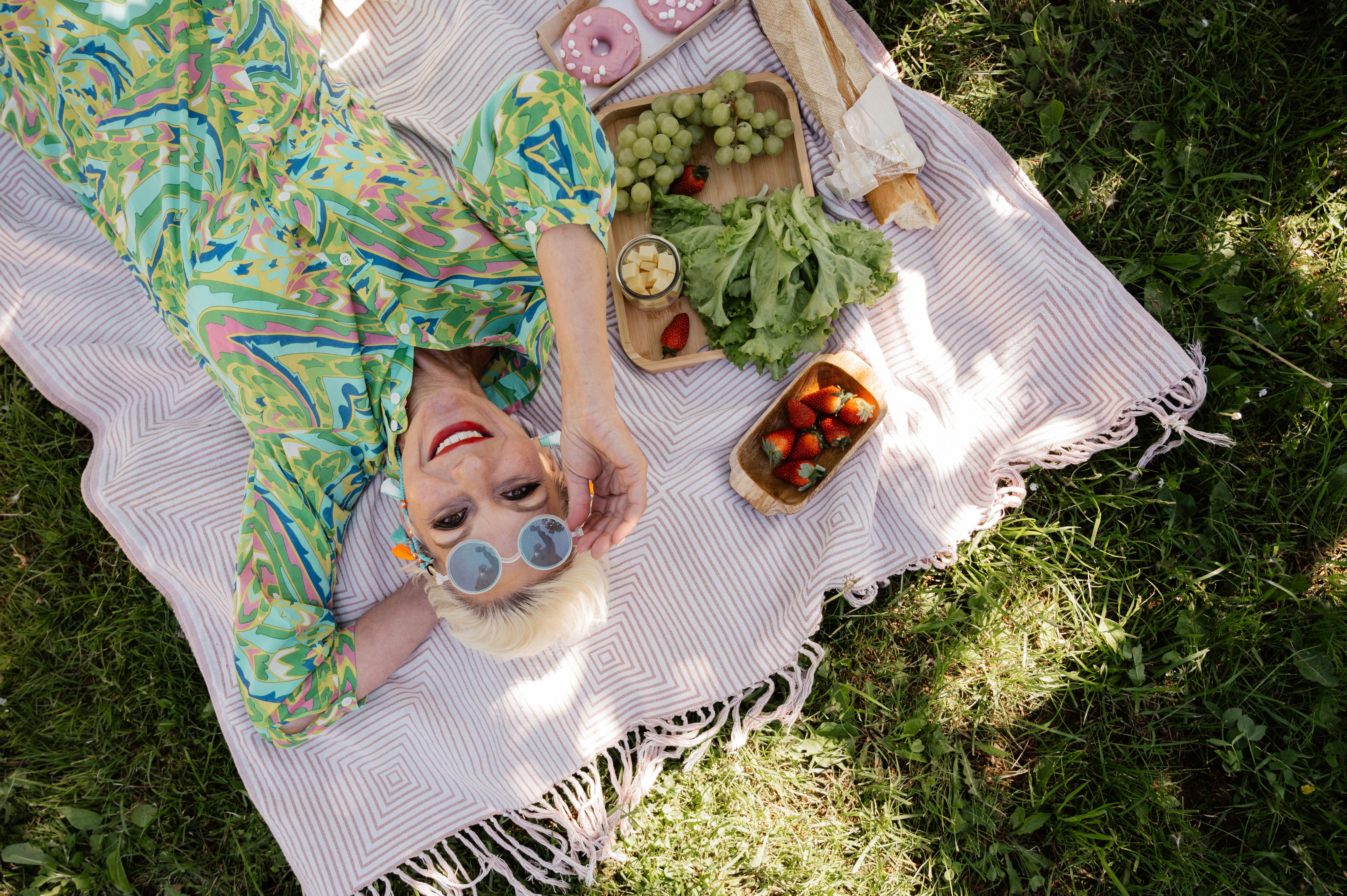 an elderly woman in green floral dress lying on a picnic blanket