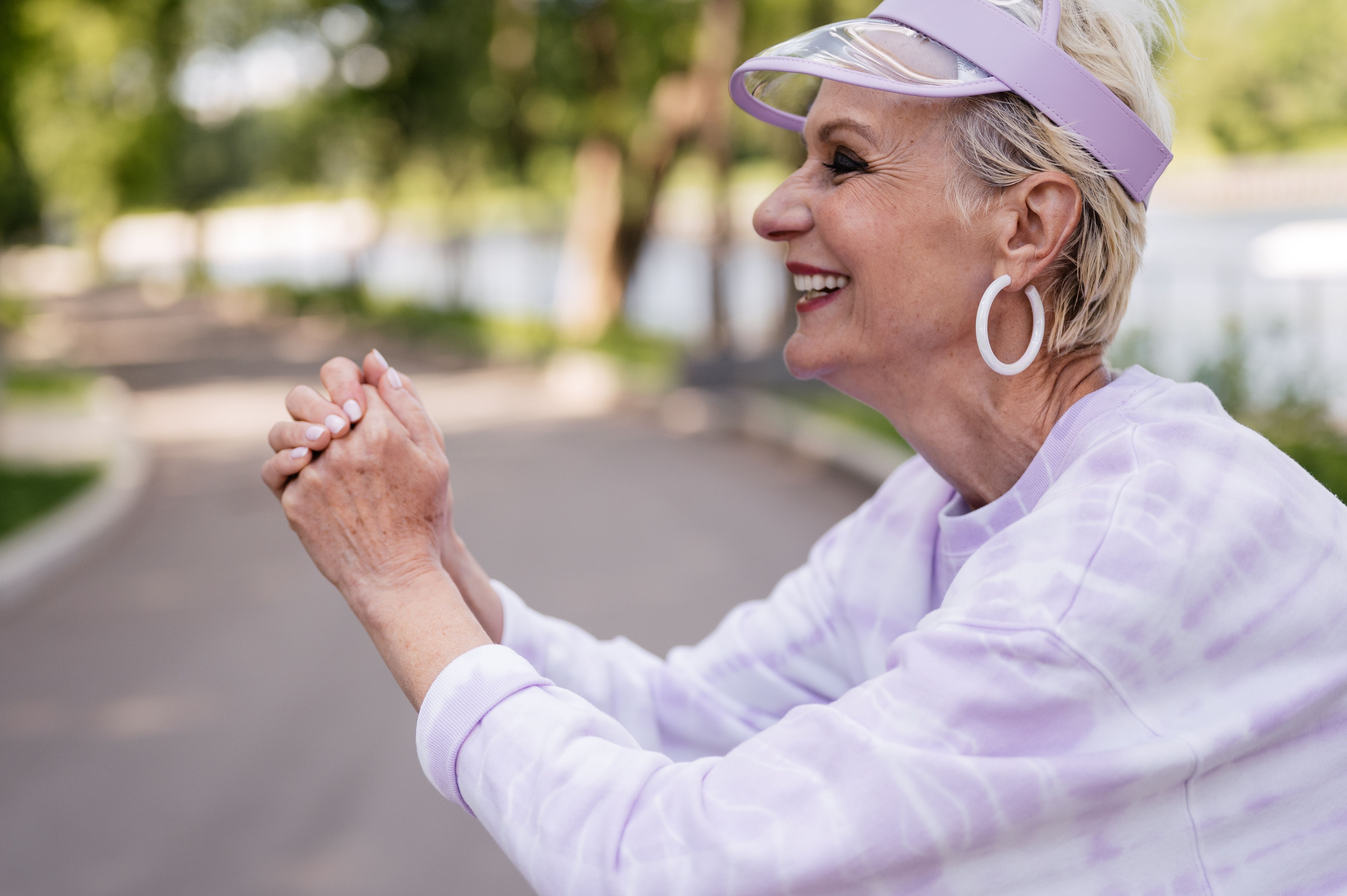 Elderly woman smiling in a stylish visor outdoors, enjoying a sunny day.