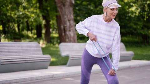 Senior woman performing outdoor exercise with a resistance band in a park setting.