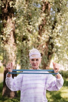 A senior woman exercises with a resistance band in a sunny park, staying fit and healthy.
