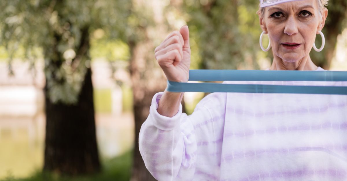 Caucasian senior woman working out with a resistance band in a park, showcasing healthy aging.