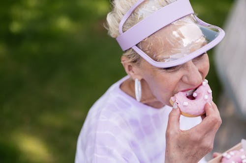  Elderly Woman in a Sun Visor Eating a Donut 